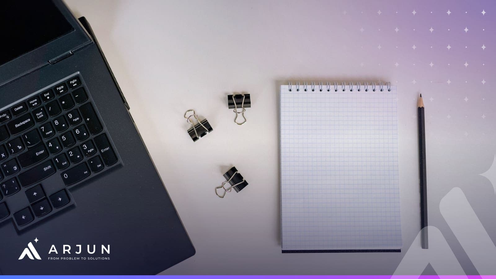 A minimal desk from above with a laptop keyboard, binder clips, a blank notepad and a pencil