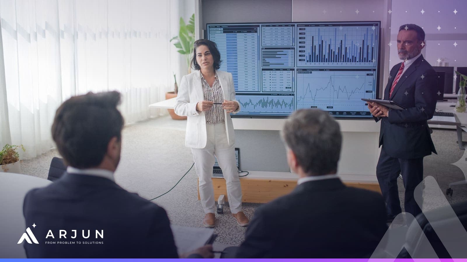 A presenter briefing colleagues in front of large screens of charts in a meeting room